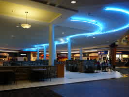 A picture of the half-empty food court in the Valley West Mall in West Des Moines, IA. Wavy blue and white neon lines the ceiling.