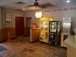 The front area of the Godfathers Pizza restaurant. The floor is brown tile, and the walls are a grey tan with wood panelling on the bottom half. Three arcade machines are pictured.