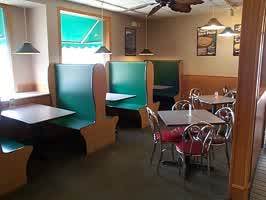 A seating area in the Godfathers Pizza restaurant. Chairs and tables are 1950's diner styled, and the booths are green on the inside with wood panelling on the outside.
