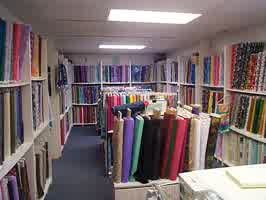 The fabric room in a quilt store in Sioux City. Fabric lines the three walls in view of the camera, with shelves containing more fabric in the middle. The fabric colors and designs vary.