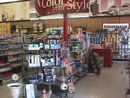 An image of a hardware store's paint counter, with a shelf containing house cleaning products in the middle.