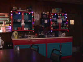 A storage cabinet in the Spink Family Restaurant. The cabinet is painted red, and the doors are painted blue. A white countertop sits on the bottom storage cabinet. The top two cabinets have string lights around the border.