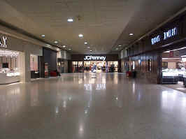 The JCPenney wing in the mall. To the sides are Kay Jewelers, Riddle's Jewelry, and closed stores. At the end is the JCPenney, its sign reflecting in the mall's tile floor.
