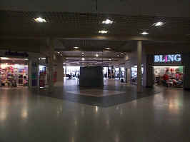 The entrance wing of the mall, shown from the center court. Stores visible include Claire's, Bling, and empty stores. In the middle is a closed cell phone booth.