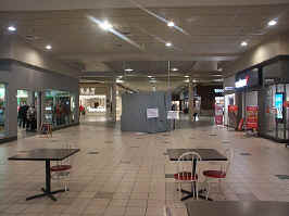 The entrance hall, looking towards the JCPenney. Tables with red and white chairs are close to the camera in the middle of the hallway. Blocking the view to JCPenney is a closed booth for Viaero Wireless.