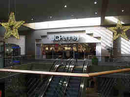 The JCPenney court from the 2nd floor, looking at the JCPenney. The escalator leads to JCPenney, lit by a skylight. Two stars hang from the ceiling.
