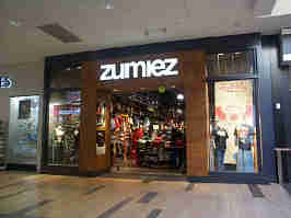 The Zumies storefront in the Oak Park Mall. A black frame surrounds windows and the woodgrain entrance, with the Zumies logo at the top.