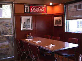 A table and chairs in the Philips Avenue Diner. The table has a  brown texture top with silver trim and the chairs have a red-brown vinyl cover with silver trim.