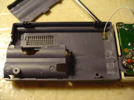 The inside of the back of the radio. The plastic is a dark purplish brown, with the battery compartment on the bottom left and a wire linking the antenna to the main circuit board at the top right.